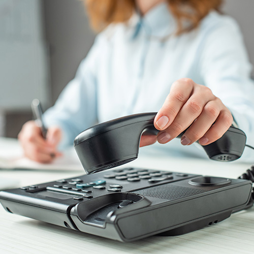 Cropped view of businesswoman putting handset on landline telephone at workplace on blurred