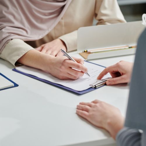 Hand of female clinician pointing at medical document while patient signing it